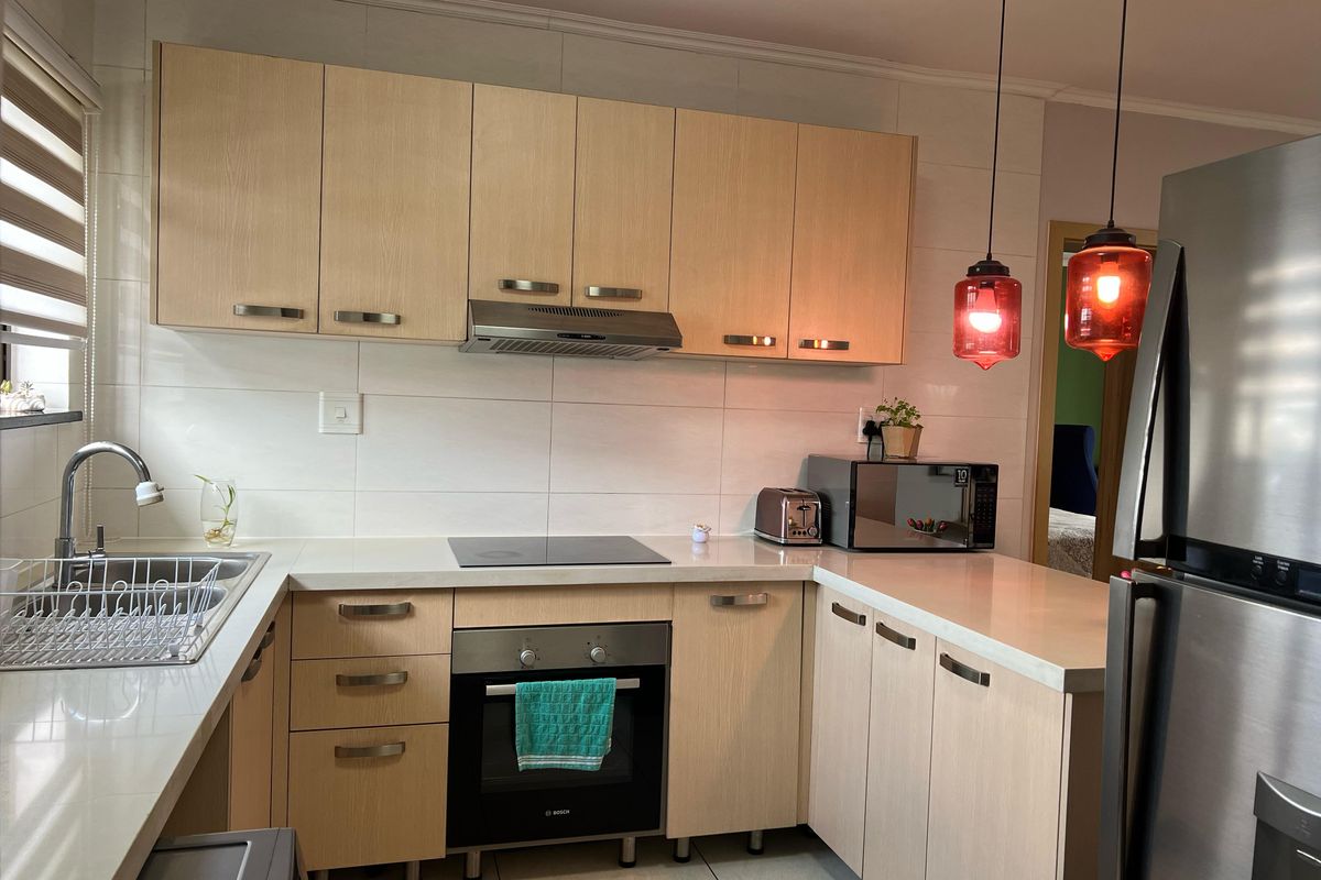 A well-maintained kitchen featuring light-wood cabinetry, stone countertops, integrated appliances, and modern pendant lighting, offering a clean and functional workspace.