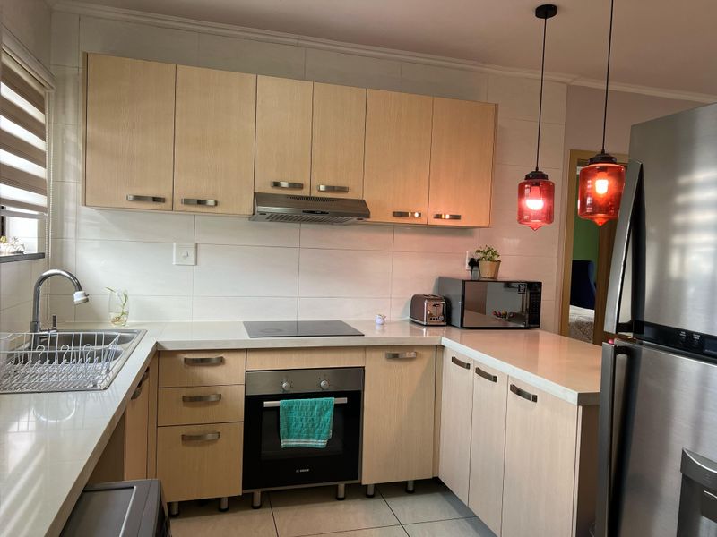 A well-maintained kitchen featuring light-wood cabinetry, stone countertops, integrated appliances, and modern pendant lighting, offering a clean and functional workspace.