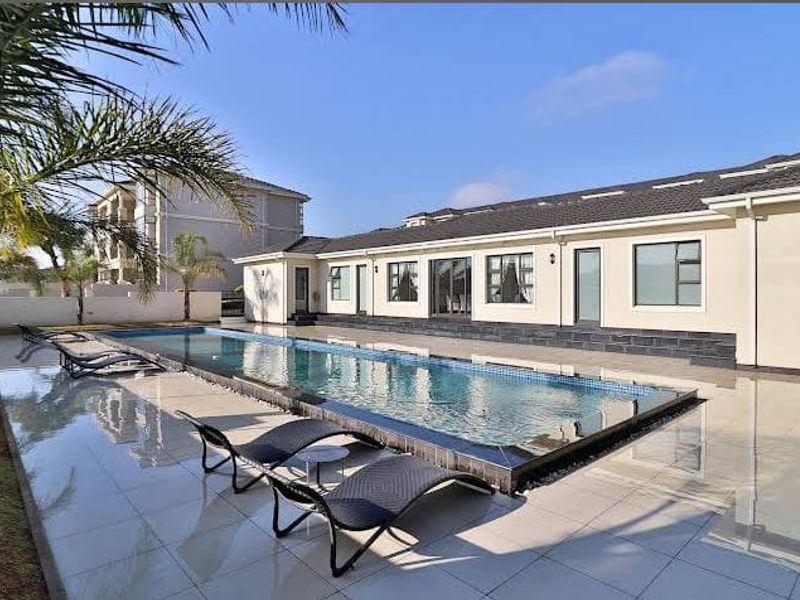 A well-maintained outdoor pool area featuring a modern swimming pool, tiled patio surround, and direct access to the apartment building via sliding doors.