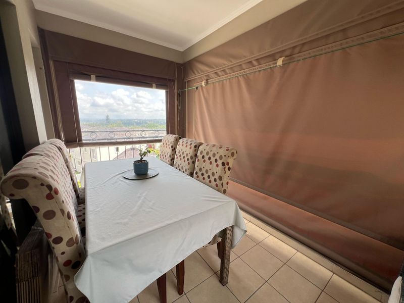 Covered balcony featuring tiled flooring, retractable privacy blinds, and a wrought iron balustrade with elevated views.