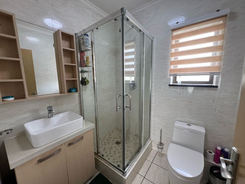 A well-maintained bathroom featuring a modern vessel sink vanity, a glass-enclosed shower, and neutral wall tiling.