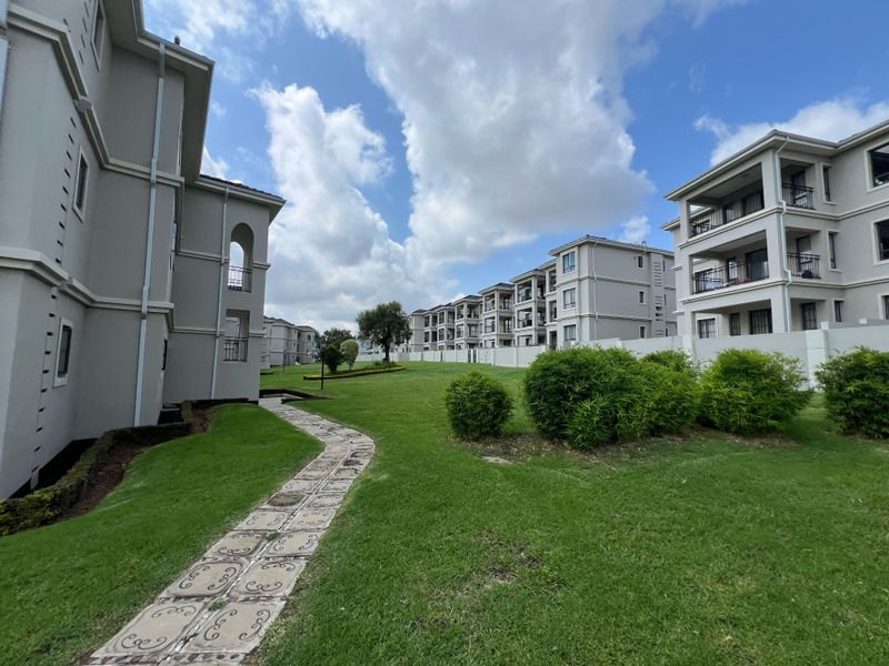 A view of the apartment complex grounds featuring well-maintained lawns, a paved stone walkway, and multi-story residential buildings with private balconies.