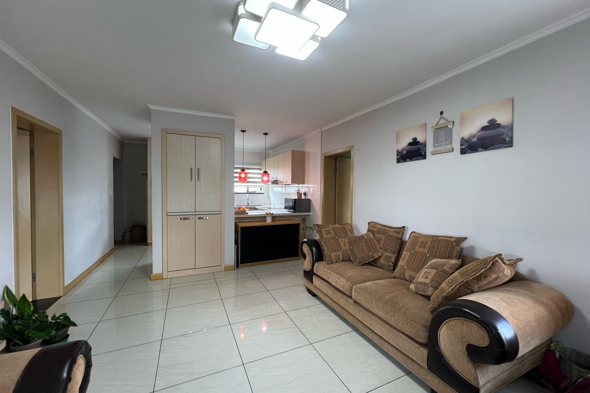 Open-plan living area featuring tiled floors, built-in cabinetry, and a modern ceiling light, seamlessly connecting to a functional kitchen space.