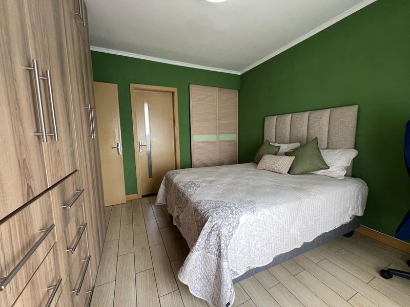 A well-maintained bedroom featuring wood-look laminate flooring, extensive built-in cabinetry, and a bold green accent wall.