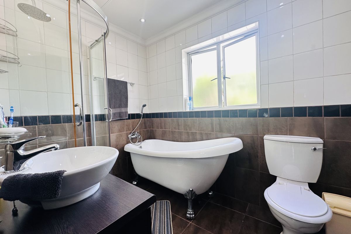 A well-appointed bathroom featuring a classic freestanding bathtub, a separate corner shower enclosure, a modern vessel sink vanity, and neutral tiled finishes.