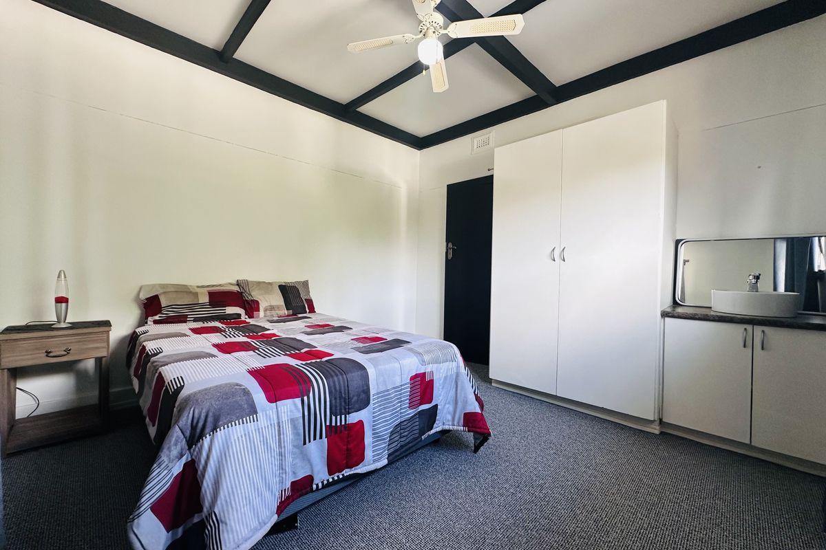 Bedroom featuring exposed ceiling beams, a ceiling fan, built-in wardrobe, and a small built-in vanity unit with a sink.