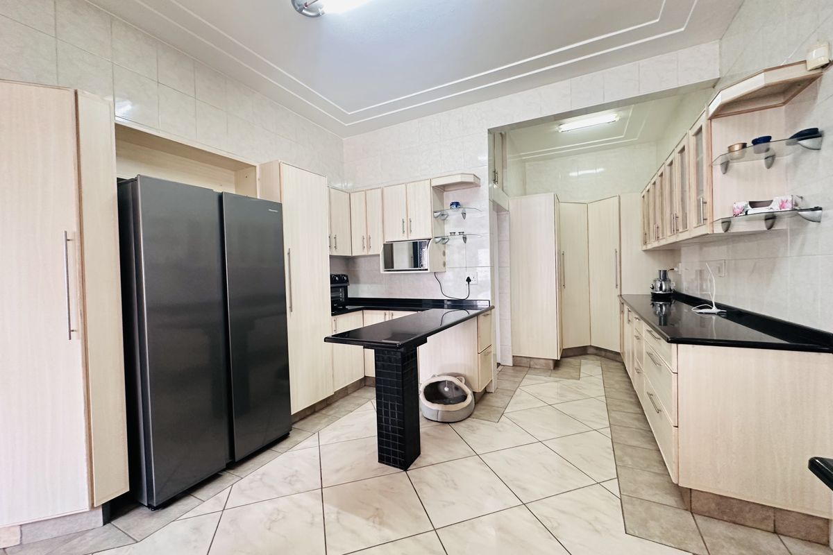 Spacious kitchen featuring light wood cabinetry, dark granite countertops, a central breakfast bar, and tiled finishes throughout.
