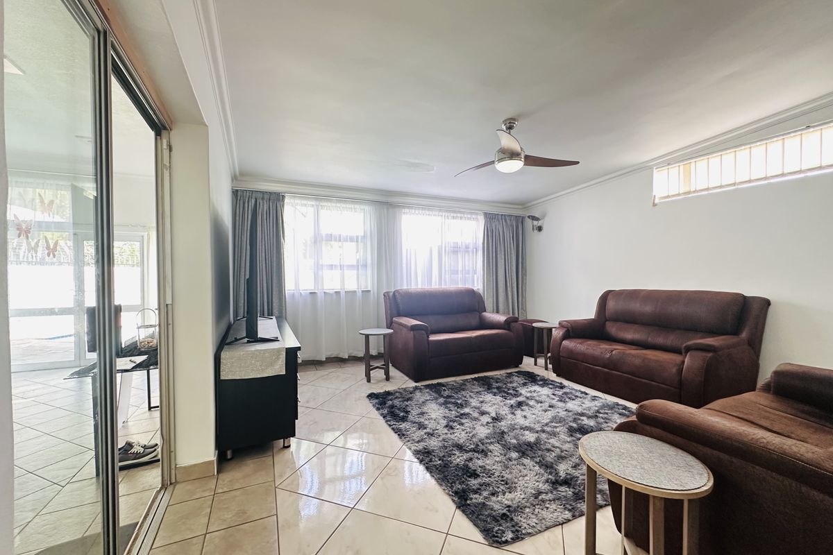A spacious living room featuring tiled flooring, a ceiling fan, and large sliding glass doors providing access to the outdoor area.