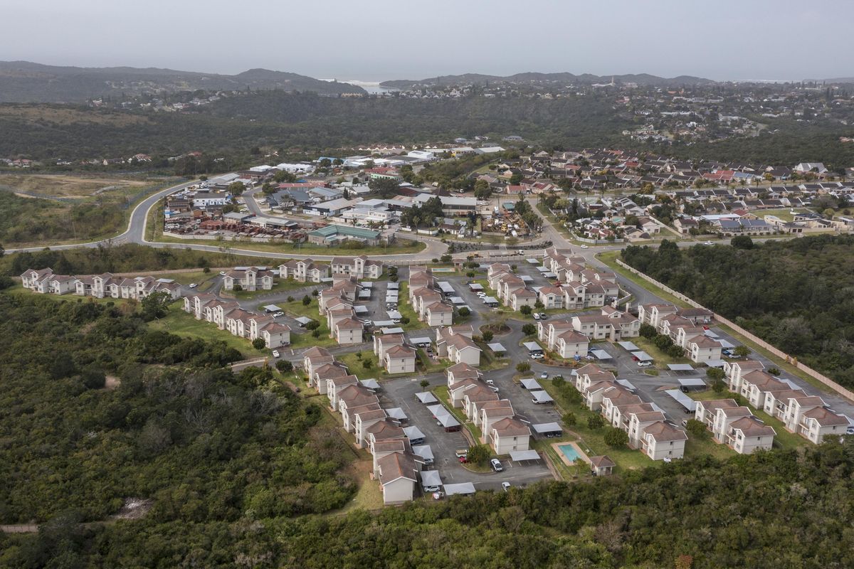 Aerial view of a residential townhouse complex featuring multiple units, paved driveways, covered parking bays, and a communal swimming pool area.