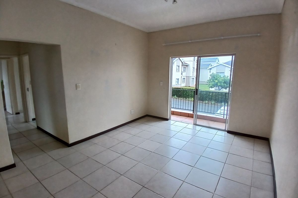 An empty living room featuring neutral tiled flooring and a sliding glass door that opens onto a small balcony.