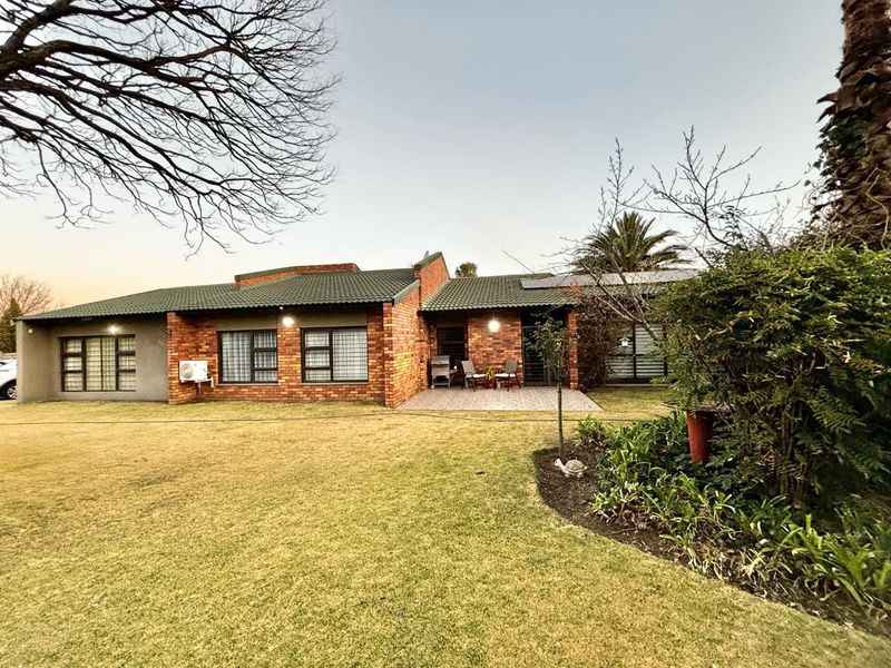 Rear view of a face brick house featuring a paved patio area, tiled roof, and established garden with solar panels installed.