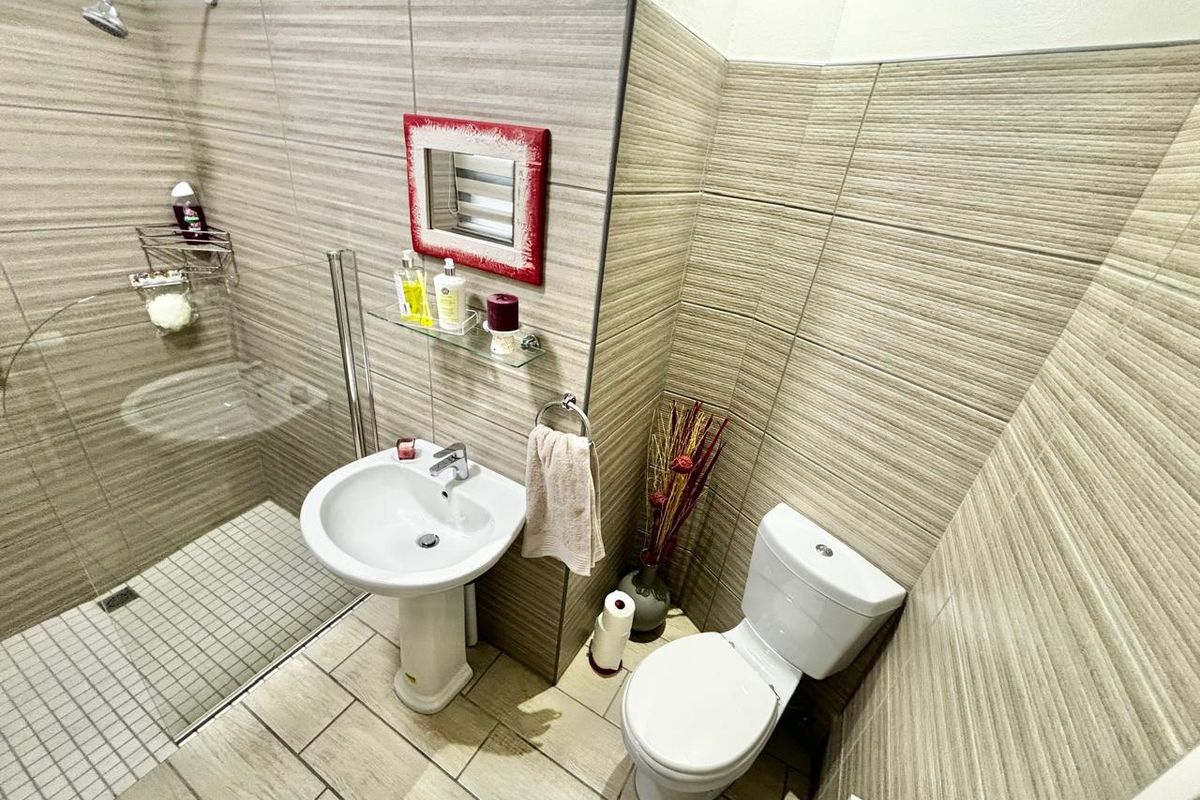 A compact bathroom featuring a pedestal basin, toilet, and a glass-enclosed shower with neutral wall and floor tiling.