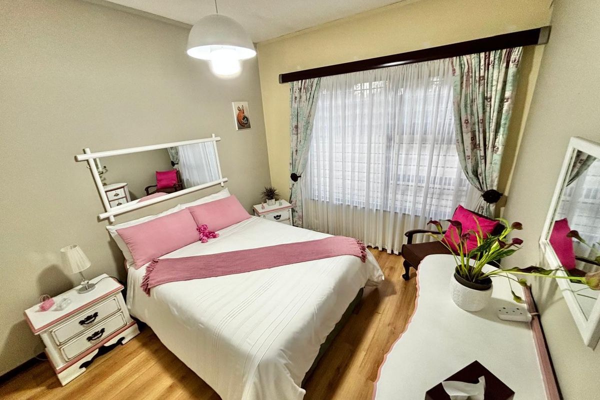 A cozy bedroom featuring laminate flooring, a central ceiling light, and a large window dressed with curtains.