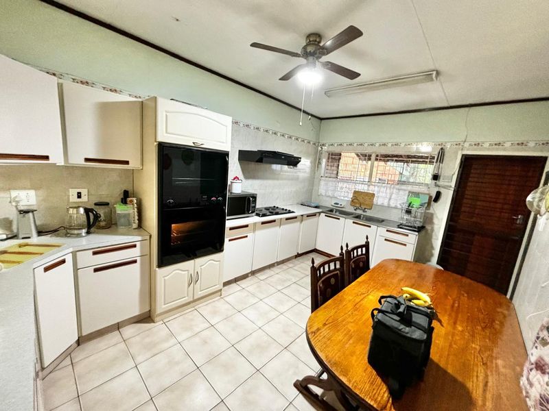 A functional kitchen featuring built-in cabinetry, an integrated oven, hob, and extractor fan, with tiled flooring and a ceiling fan.