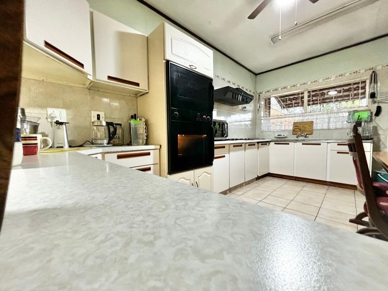 A functional kitchen featuring white built-in cabinetry, laminate countertops, a built-in oven, and tiled flooring, offering a classic layout with potential for modernization.