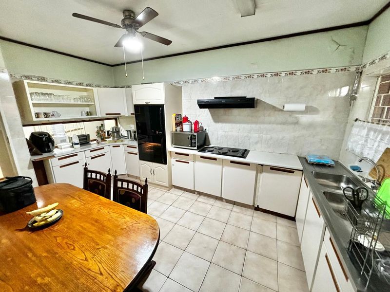 A functional kitchen featuring built-in cabinetry, a double basin sink, electric hob, and extractor fan, with tiled flooring and backsplash throughout.