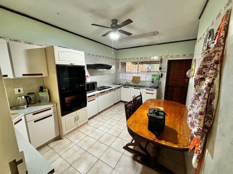 A functional kitchen featuring built-in cabinetry, an integrated oven, hob, extractor fan, and tiled flooring with a dedicated dining area.