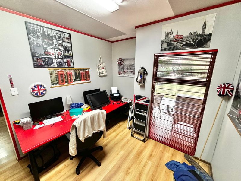 A functional home office space featuring laminate flooring, built-in desk area, and direct access to the outdoor area through a glass door with blinds.