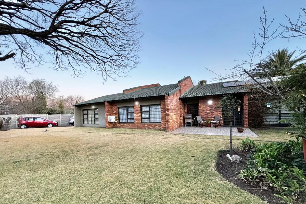 A well-maintained face brick house featuring a tiled roof, paved patio area, and a spacious rear garden with established landscaping.