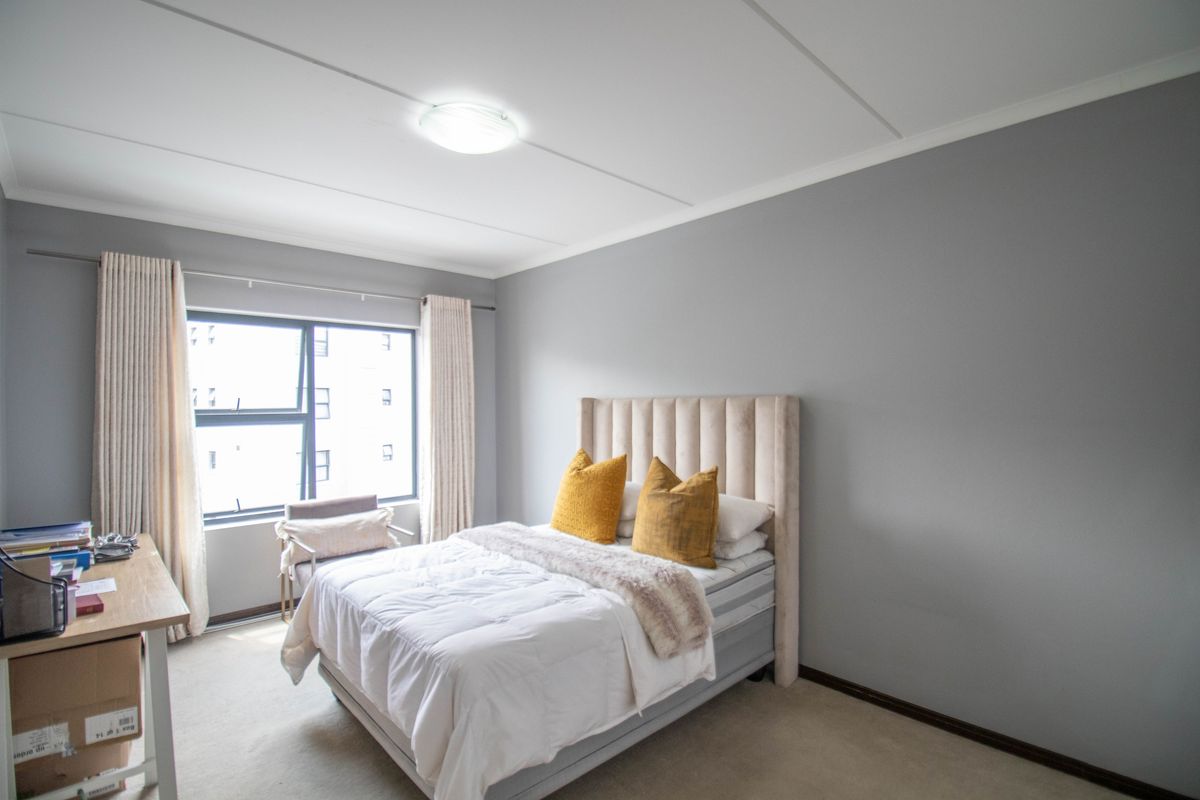 A well-lit bedroom featuring neutral grey walls, carpeted flooring, and a large aluminium-framed window providing natural light.