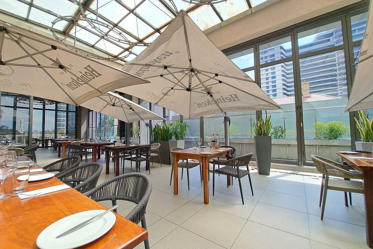 A bright, covered patio area featuring a glass roof, large sliding doors, and tiled flooring, suitable for outdoor dining and entertainment.
