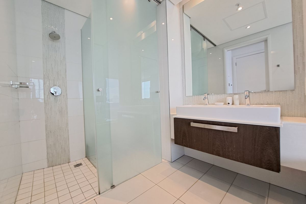 Modern bathroom featuring a spacious walk-in shower with frosted glass, a sleek wall-mounted double vanity, and elegant mosaic tile accents.