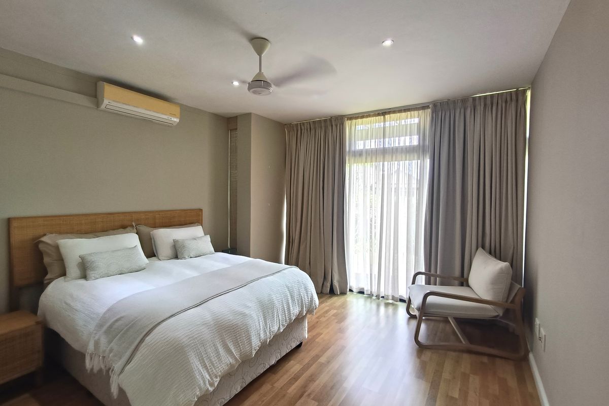 A well-maintained bedroom featuring laminate flooring, a ceiling fan, split-system air conditioning, and large sliding glass doors providing natural light.