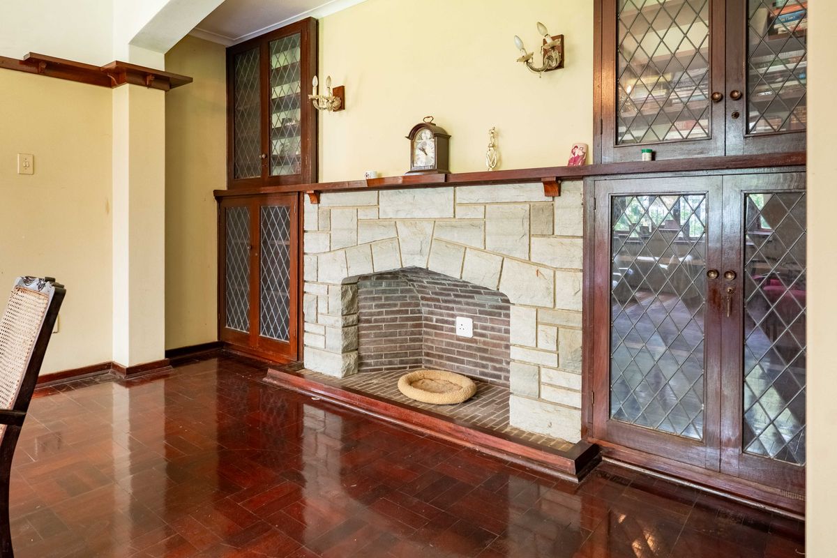 Living room featuring a prominent stone fireplace with brick hearth, flanked by custom built-in wooden cabinetry with leaded glass detailing and polished parquet flooring.