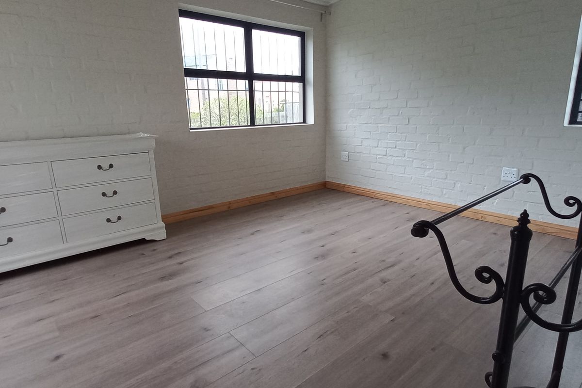 A bright bedroom featuring painted brick walls, light wood-look laminate flooring, and security bars on the windows.