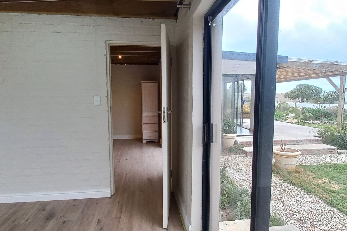 Interior view looking through a doorway into an adjacent room, featuring light wood-look flooring, painted brick walls, and large sliding glass doors to the garden.