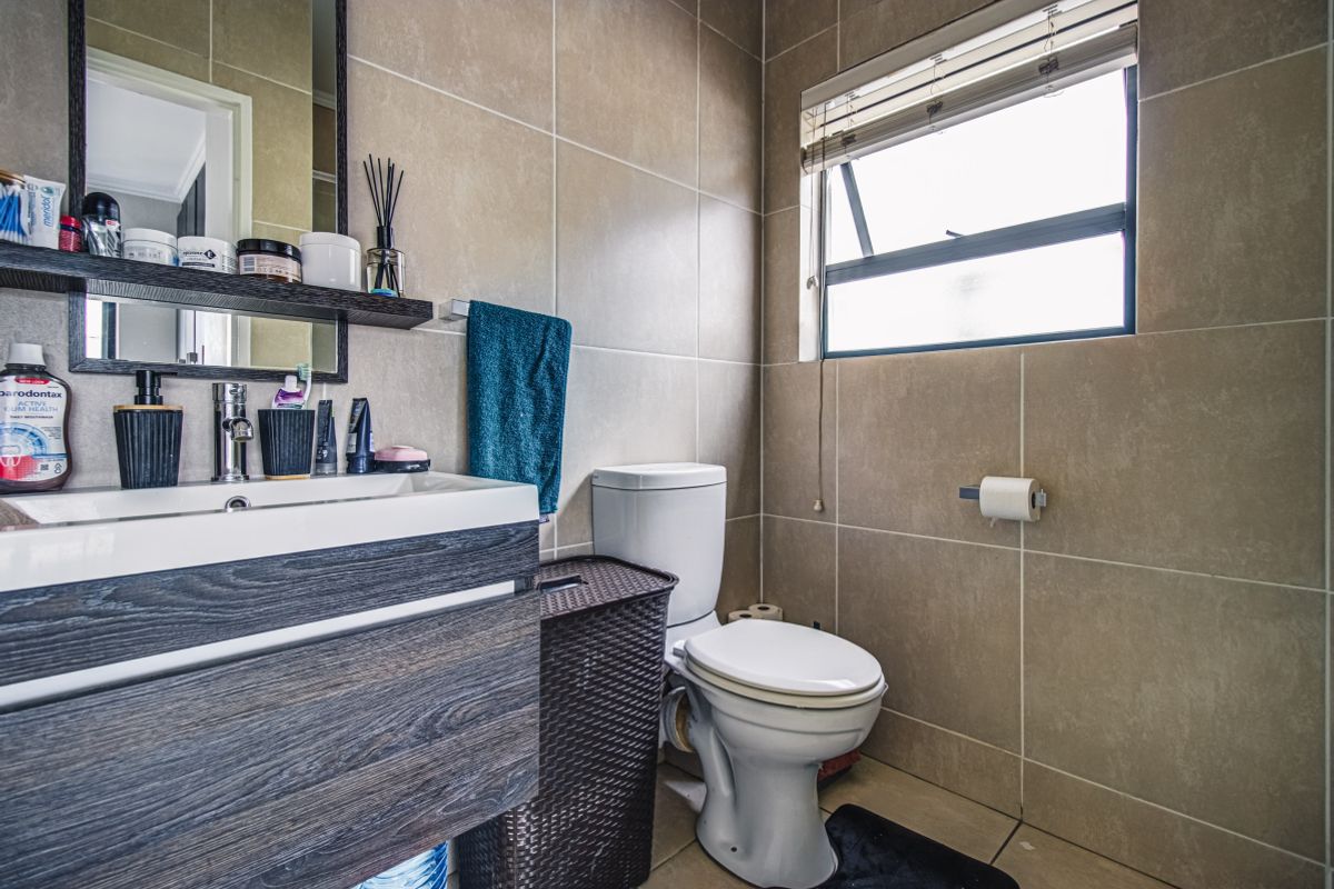 A modern bathroom featuring floor-to-ceiling neutral wall tiles, a contemporary vanity unit with integrated basin, and a standard toilet.
