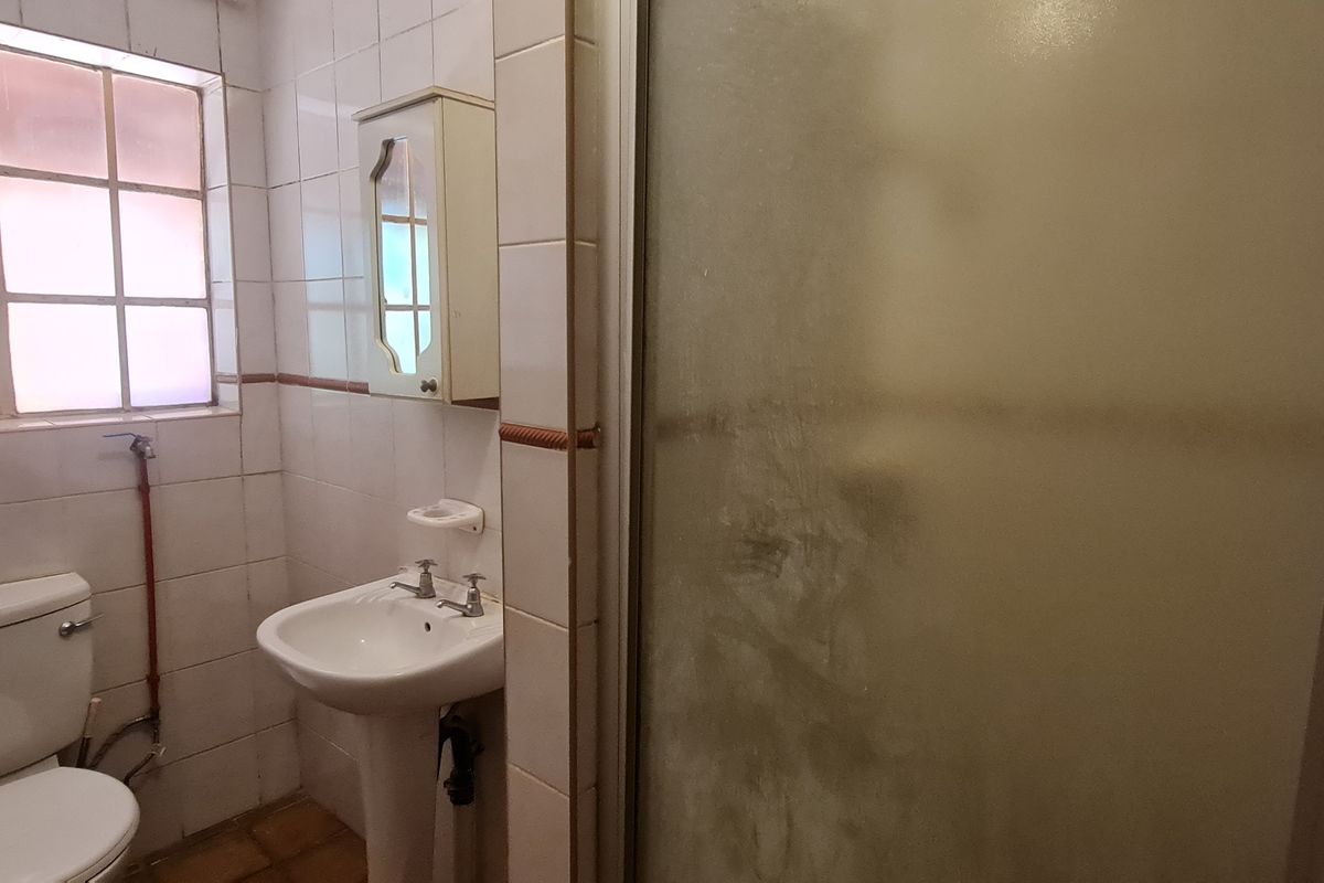 A functional bathroom featuring a pedestal basin, toilet, and a shower enclosure with tiled walls and a window for natural light.