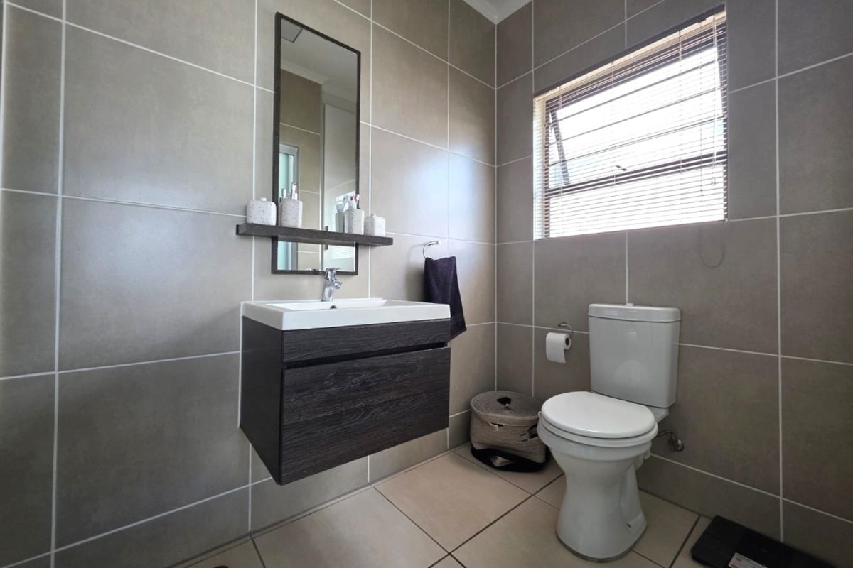 Modern bathroom featuring floor-to-ceiling neutral tiling, a wall-mounted vanity with integrated basin, mirror, and a standard toilet.