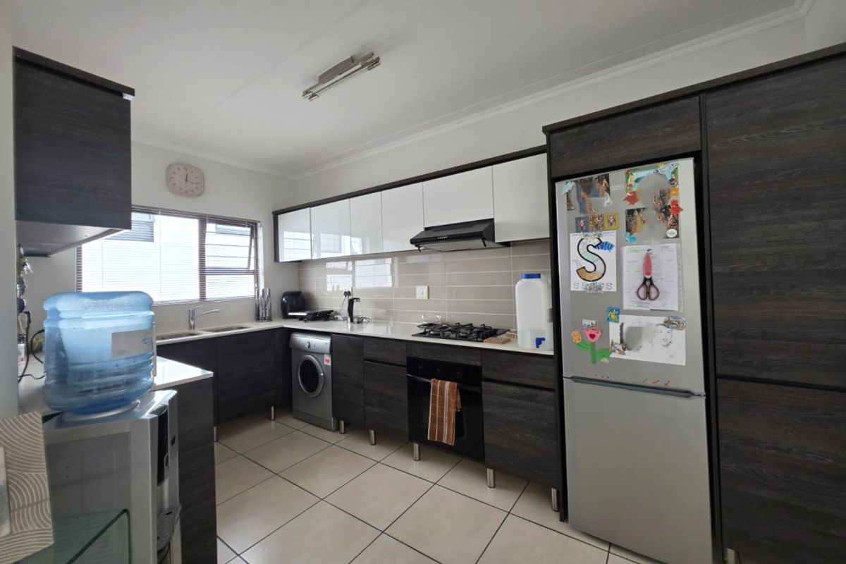 Modern kitchen featuring dark wood-grain cabinetry, white upper cabinets, tiled flooring, built-in oven, gas hob, extractor fan, and integrated laundry plumbing.