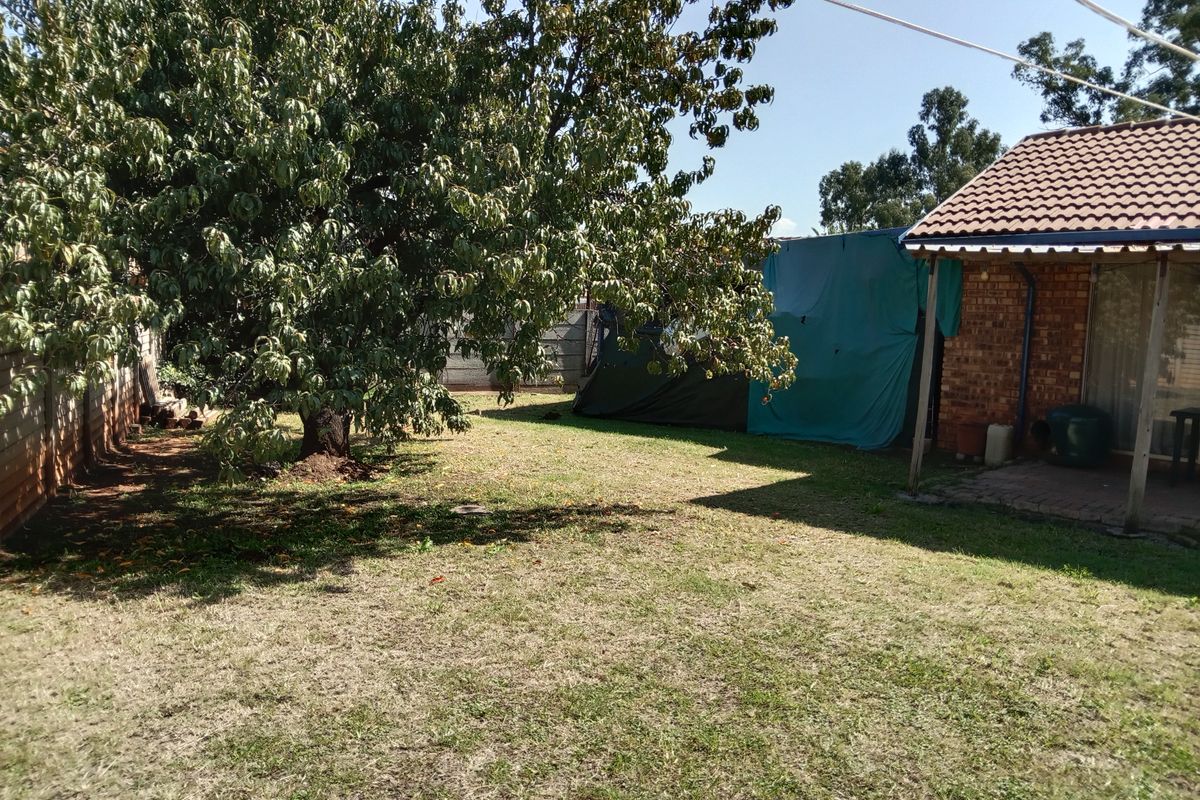 A view of the rear garden featuring a brick facade, tiled roof, and a concrete patio area with a large mature tree.