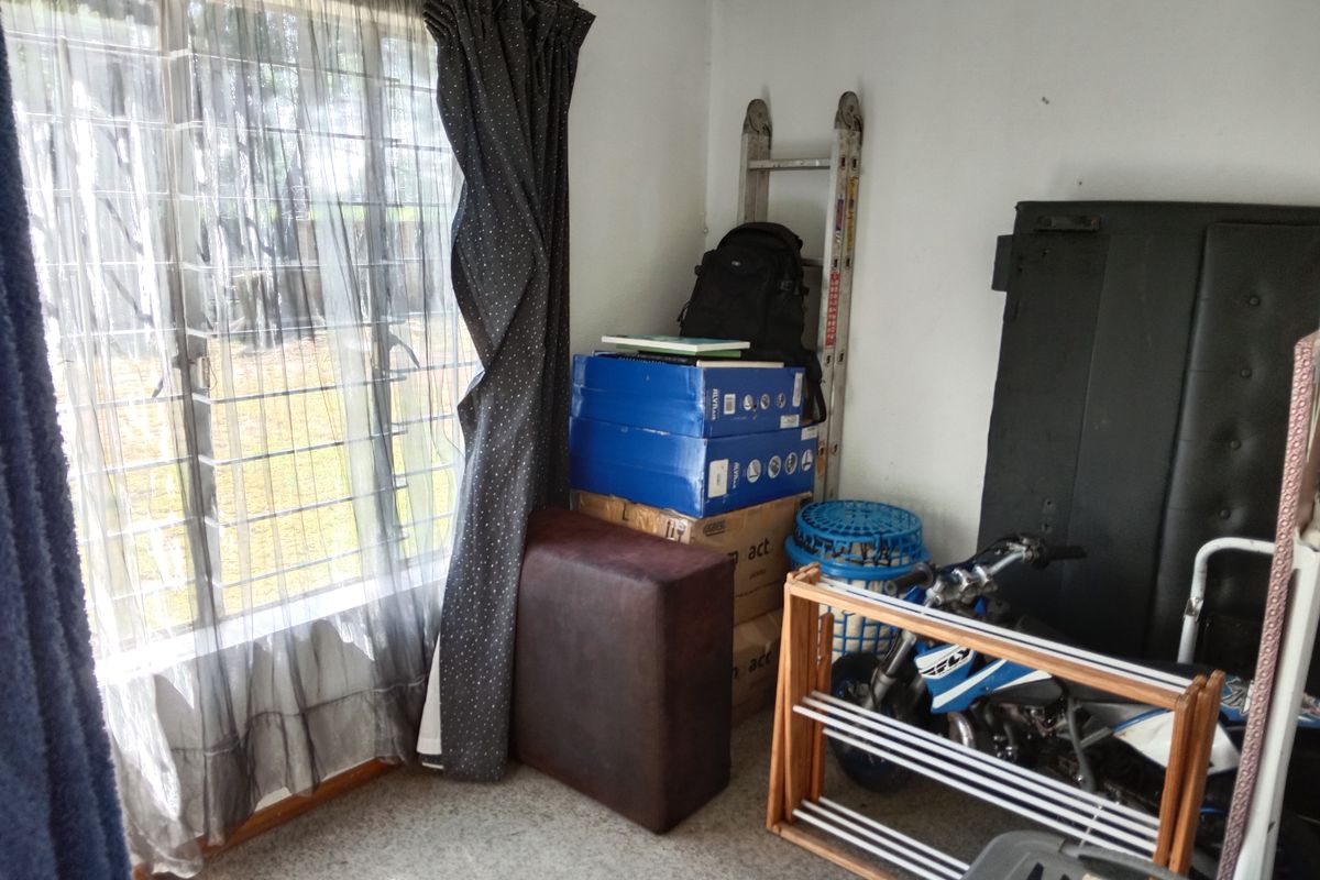A bedroom space featuring a window with security bars and curtain rails, currently utilized for storage.