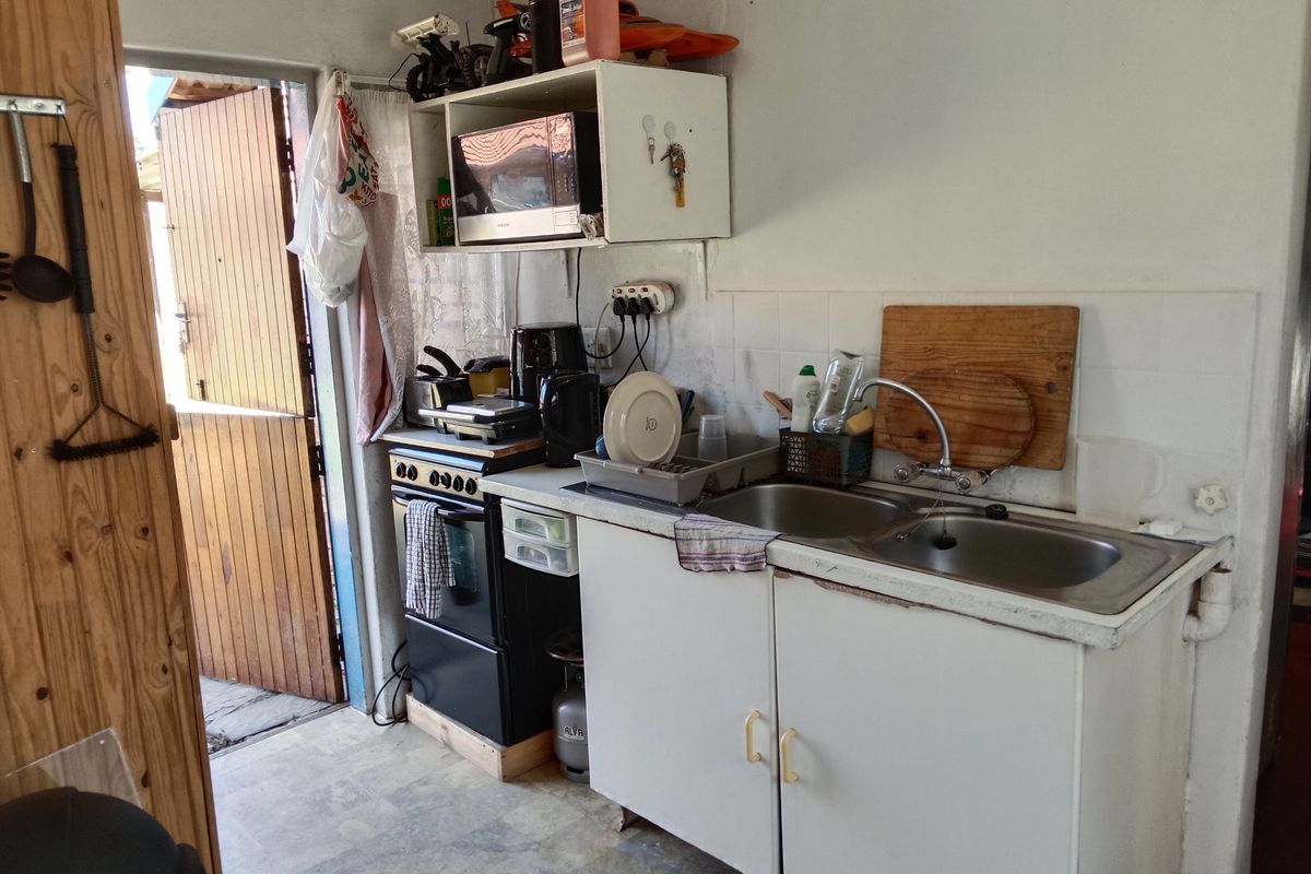 A compact, functional kitchen area featuring a double sink, tiled backsplash, and basic cabinetry, requiring cosmetic updates to improve its overall condition.