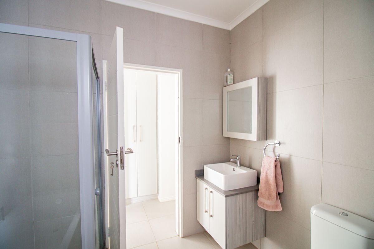 A modern bathroom featuring a glass shower enclosure, a contemporary vessel sink with vanity cabinet, and neutral wall tiling.