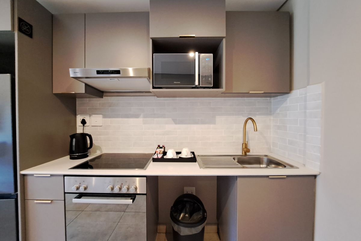 Modern compact kitchen featuring grey cabinetry, subway tile backsplash, brass faucet, integrated oven, hob, extractor fan, and built-in microwave.