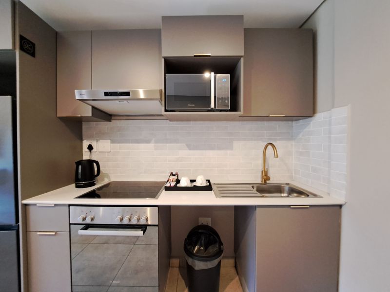 Modern compact kitchen featuring grey cabinetry, subway tile backsplash, brass faucet, integrated oven, hob, extractor fan, and built-in microwave.