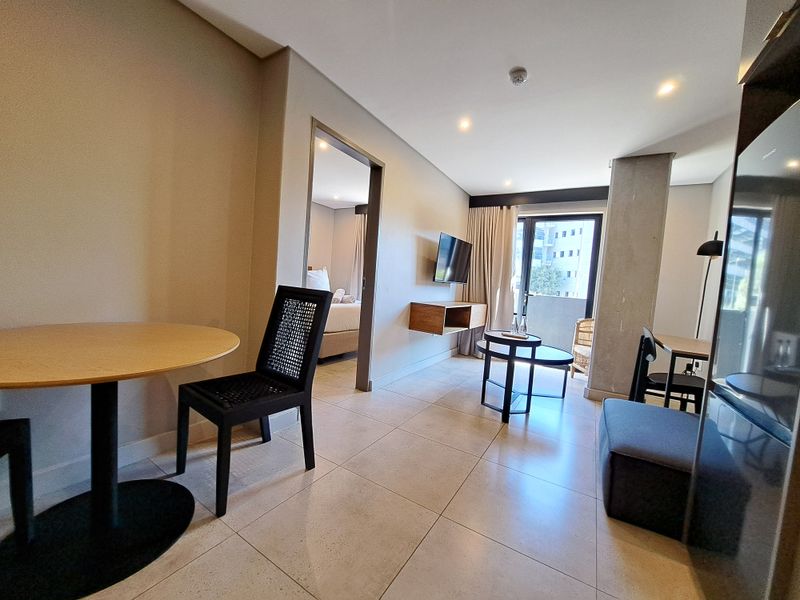 Modern open-plan living area featuring large format floor tiles, recessed lighting, and an exposed concrete column, with seamless access to a private balcony.
