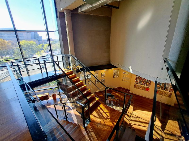 Modern industrial-style interior featuring a prominent timber staircase with glass balustrades, floor-to-ceiling windows, and exposed concrete architectural elements.