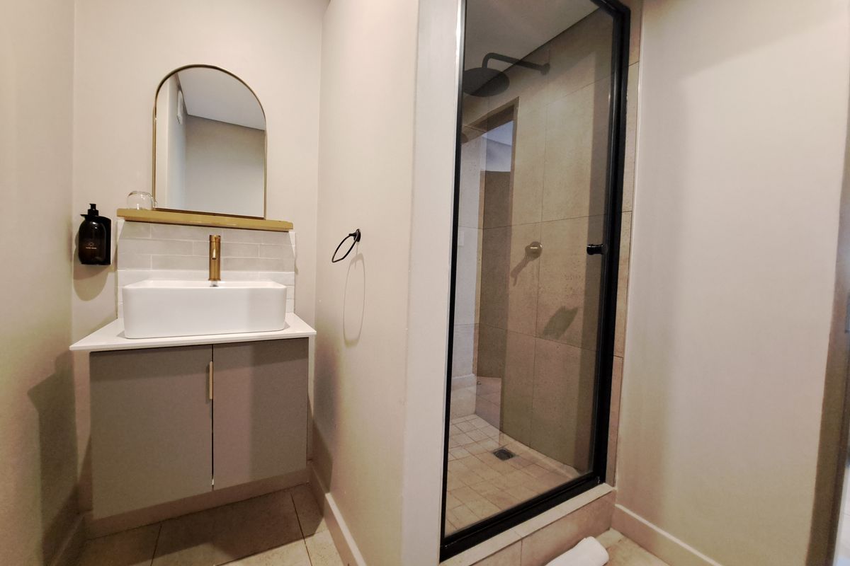Modern bathroom featuring a vanity with a vessel sink, brass fixtures, an arched mirror, and a walk-in shower with a glass enclosure.