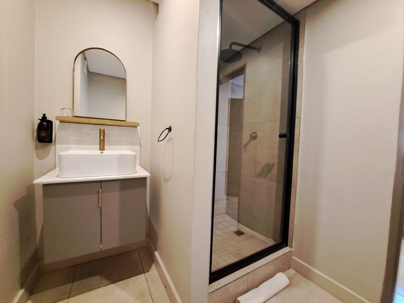 Modern bathroom featuring a vanity with a vessel sink, brass fixtures, an arched mirror, and a walk-in shower with a glass enclosure.