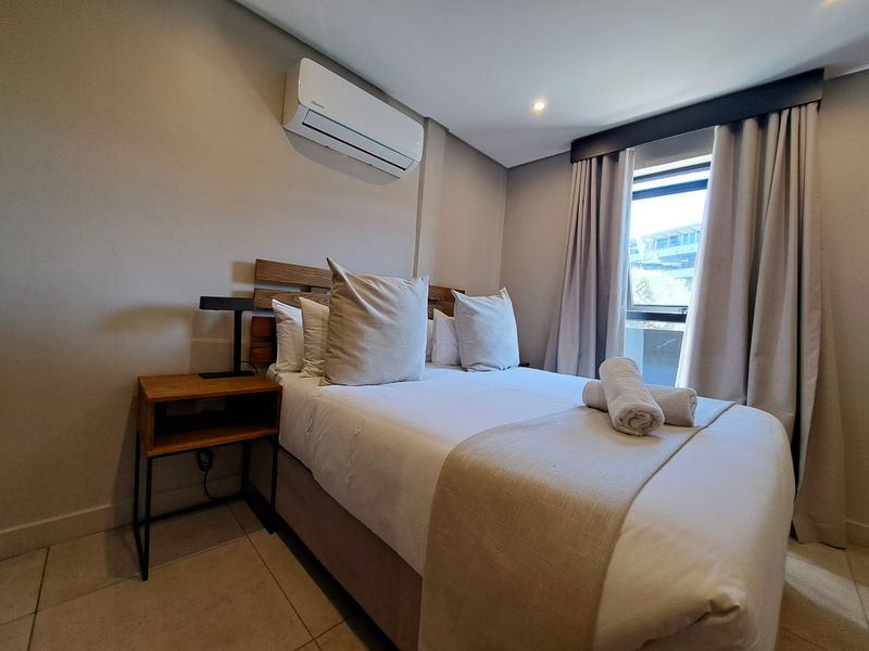 A well-maintained bedroom featuring tiled flooring, recessed lighting, and a wall-mounted air conditioning unit.
