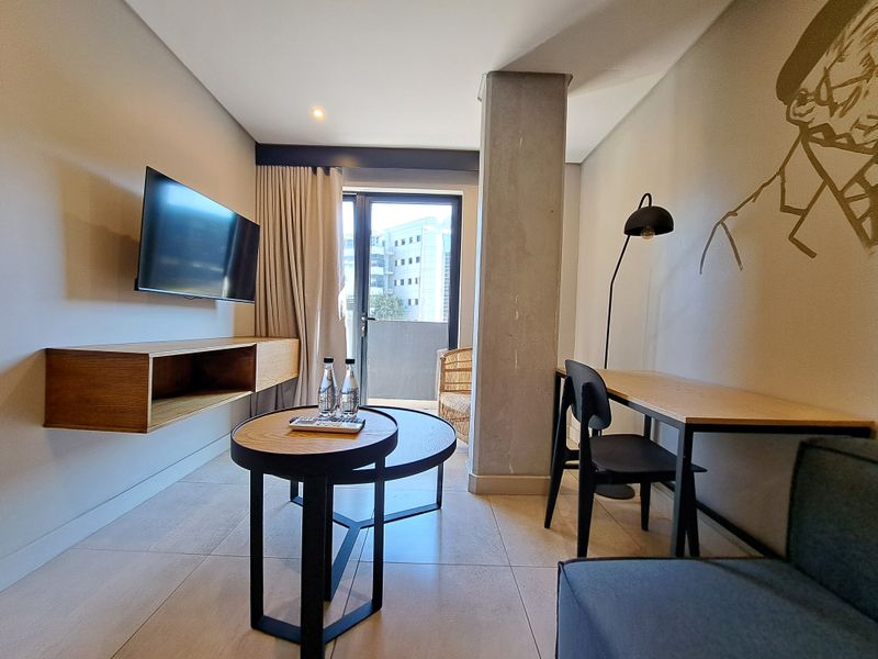 Modern living area featuring tiled flooring, an exposed concrete column, and a floating timber shelf with direct access to a private balcony.