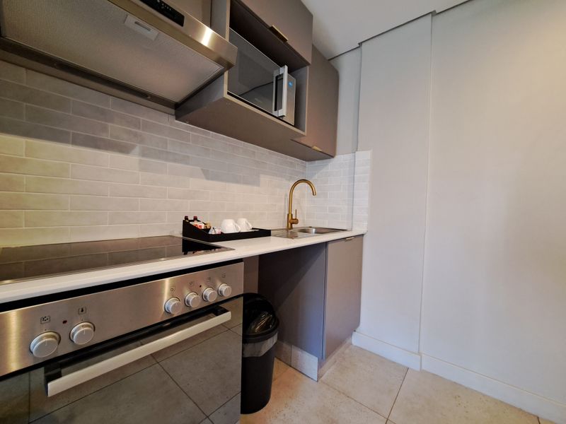 Modern compact kitchen featuring sleek grey cabinetry, subway tile backsplash, integrated appliances, and a stylish brass faucet.