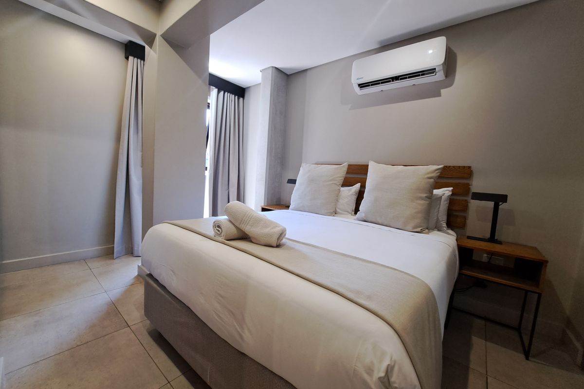 A modern, well-maintained bedroom featuring neutral tones, tiled flooring, and a wall-mounted air conditioning unit.
