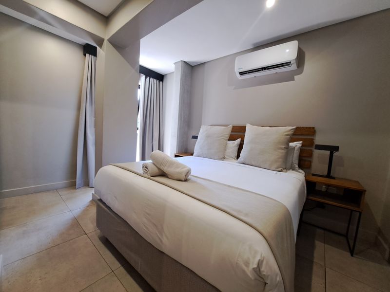 A modern, well-maintained bedroom featuring neutral tones, tiled flooring, and a wall-mounted air conditioning unit.