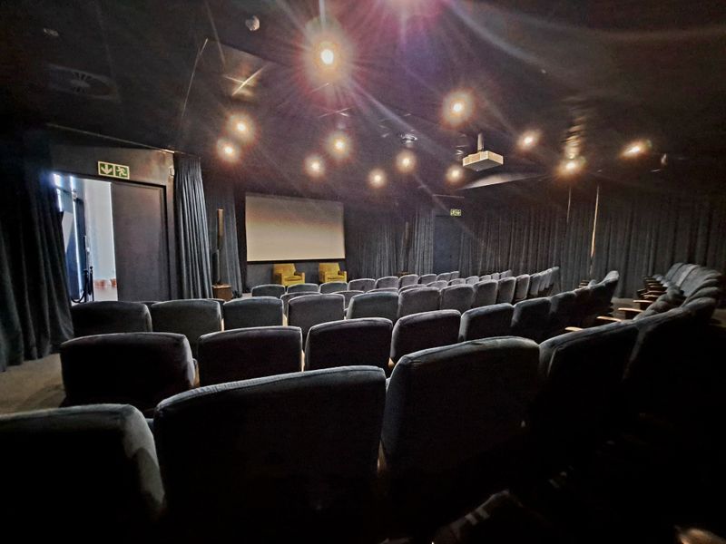 A dedicated private cinema room featuring tiered seating, a large projection screen, professional lighting, and acoustic wall curtains.